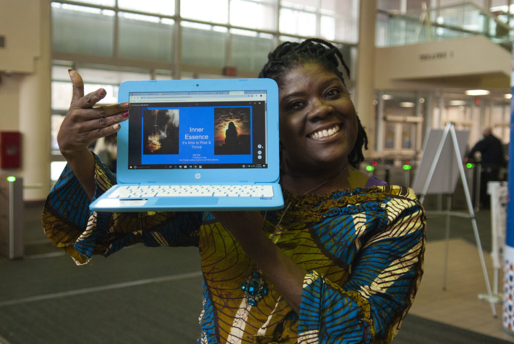 Woman of African descent proudly shows off a laptop with slideshow created during class