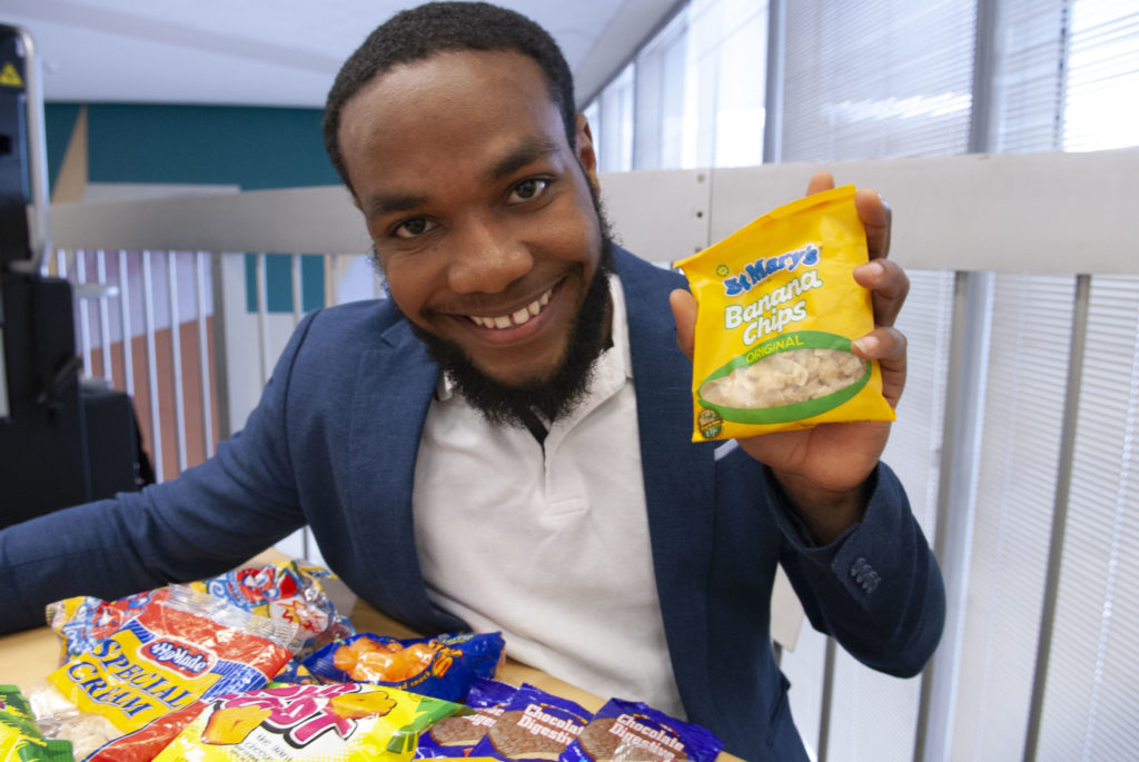 Black male smiles and holds up a package of banana chips