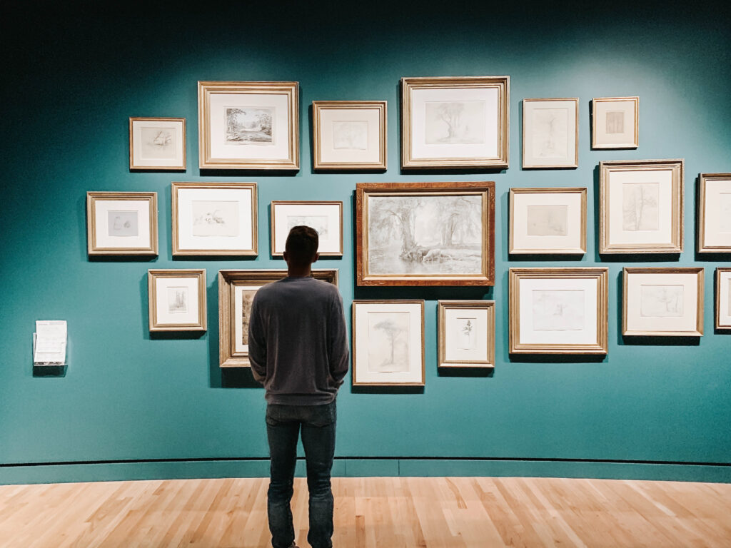 Man gazes at framed sketches on an art galley wall